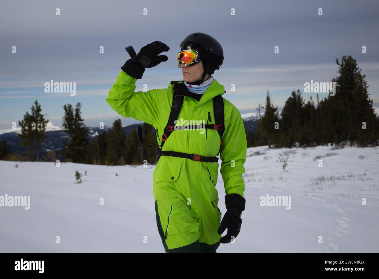 Mann in hellsäuregrünem Snowboardanzug, schwarzen warmen Handschuhen, orangen Brillen, Helm und Rucksack Skier Outfit, reicht Hand in Richtung seines Hades. Erkundet s Stockfoto