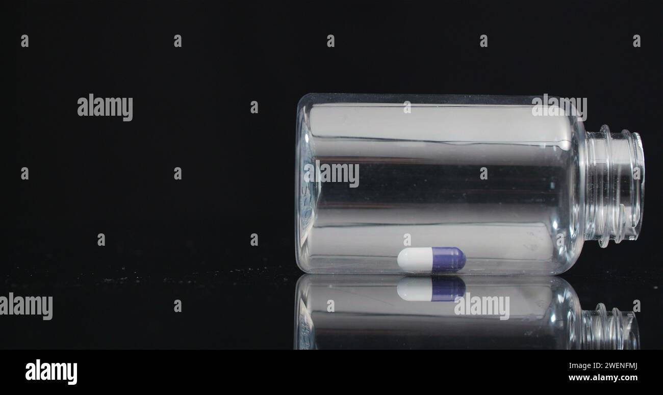 Einzelne medizinische Pille in der kleinen Flasche, die auf schwarzem Hintergrund rotiert. Stockfoto