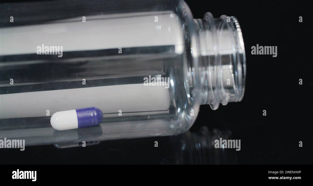 Einzelne medizinische Pille in der kleinen Flasche, die auf schwarzem Hintergrund rotiert. Stockfoto