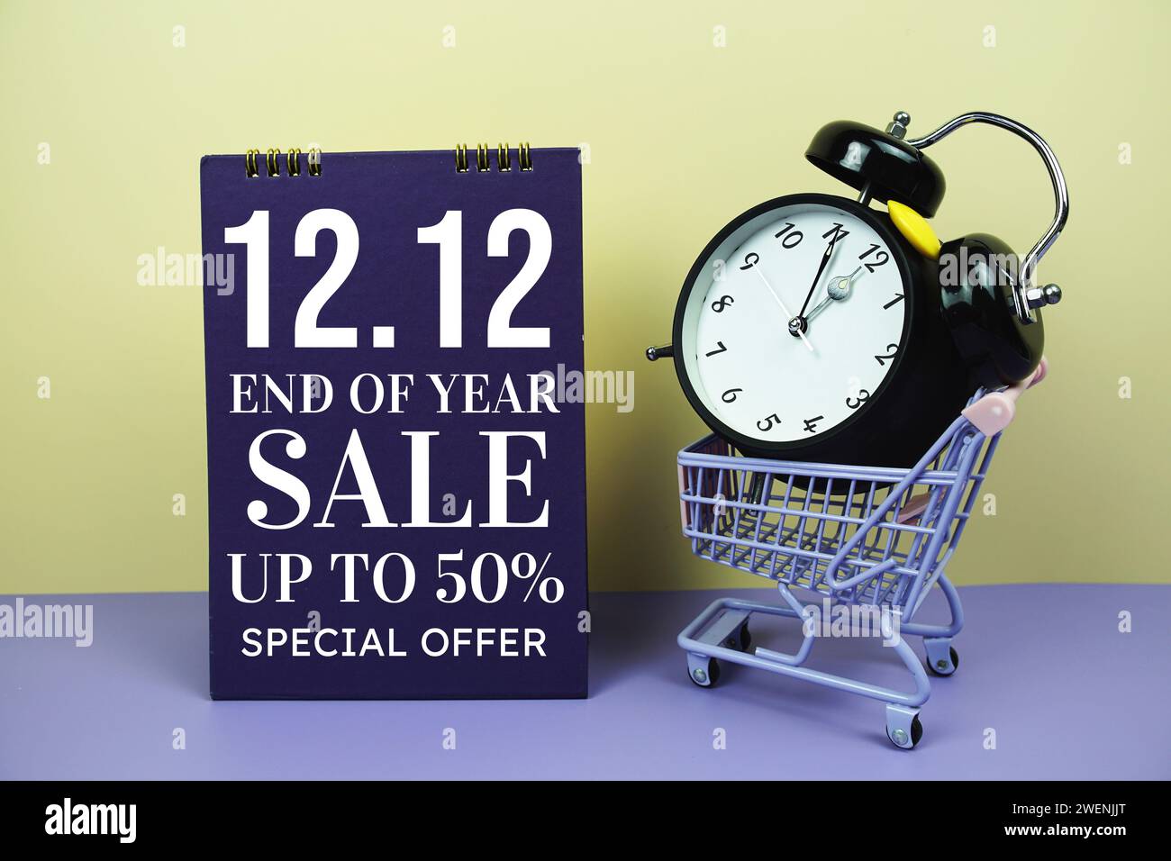 12,12 Verkaufsförderung zum Jahresende mit Einkaufswagen und Alarmklammer auf gelbem Hintergrund, Hintergrund Geschäftskonzept Stockfoto