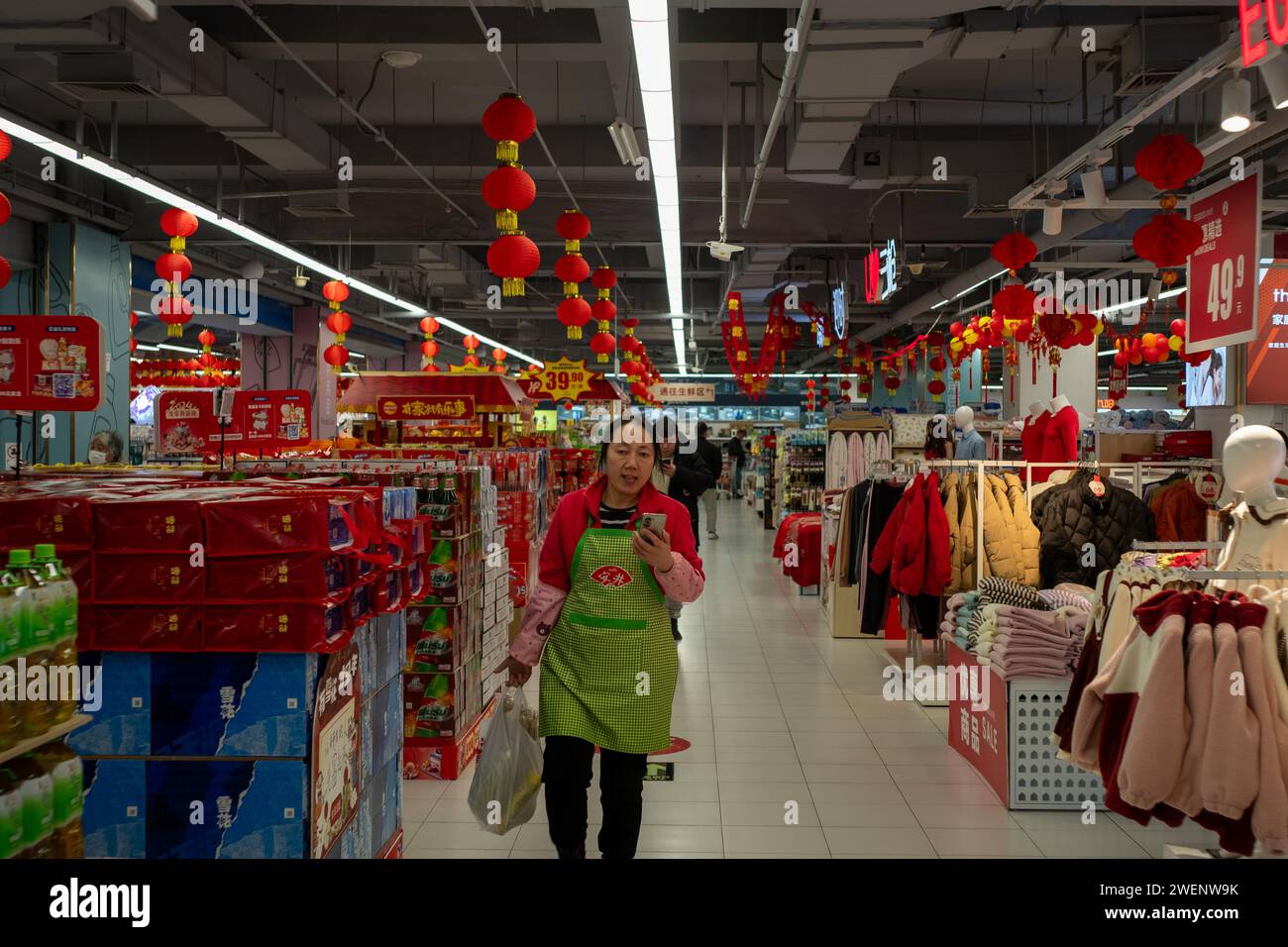 Ein Verkäufer hält eine Tasche mit Waren in einer Hand, während er in einem Einkaufszentrum in Peking mit seinem Handy spricht. Januar 2024 Stockfoto