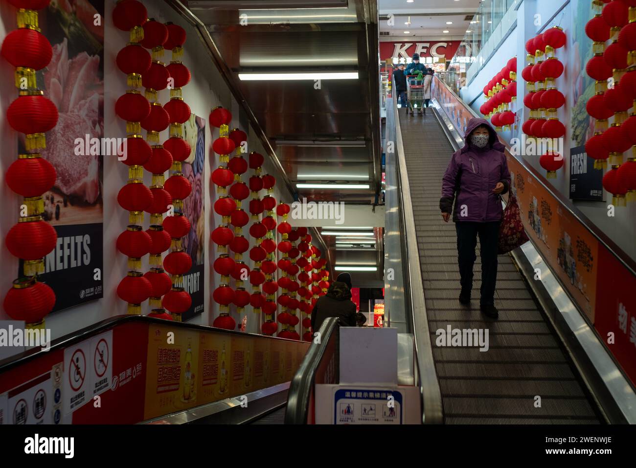 Eine Frau nimmt die Rolltreppe, um im Einkaufszentrum einkaufen zu gehen, mit roten Laternen, die auf beiden Seiten in Peking hängen. Januar 2024 Stockfoto