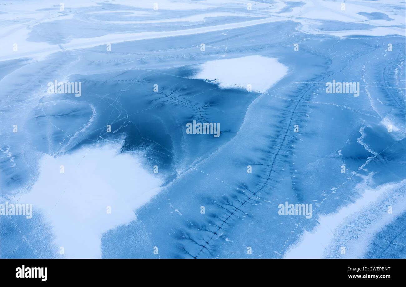 Gefrorene Seenoberfläche mit Schnee bedeckt mit Rissen im Eis. Aus der Vogelperspektive. Stockfoto