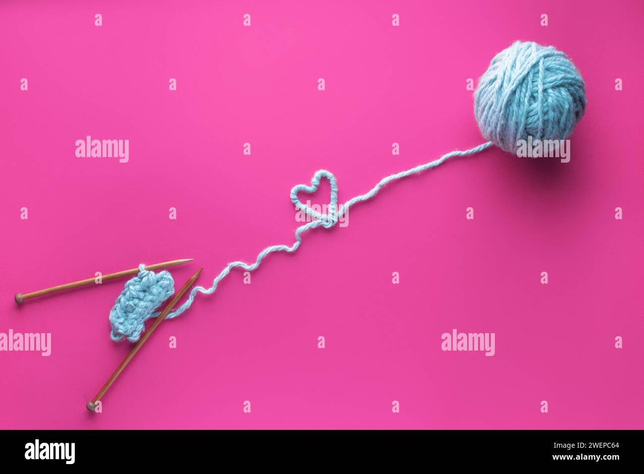 Blauer Fadenkugel und Stricknadeln auf rosa Hintergrund. Das Konzept der Liebe zu Handarbeit und Stricken. Herz aus Gewinde. Stockfoto