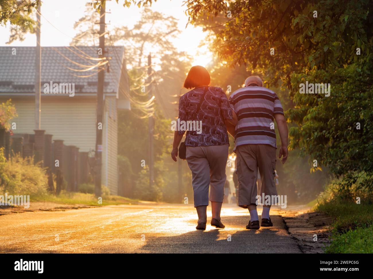 Ein älteres Paar läuft die Straße entlang und hält Hände. Spaziergang von alten Leuten bei Sonnenuntergang an einem Sommerabend. Stockfoto