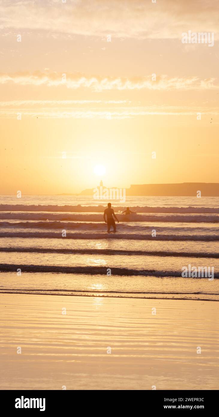 Menschen, die im Meer baden, mit Insel dahinter bei Sonnenuntergang in Essaouira, Marokko, 26. Januar 2024 Stockfoto