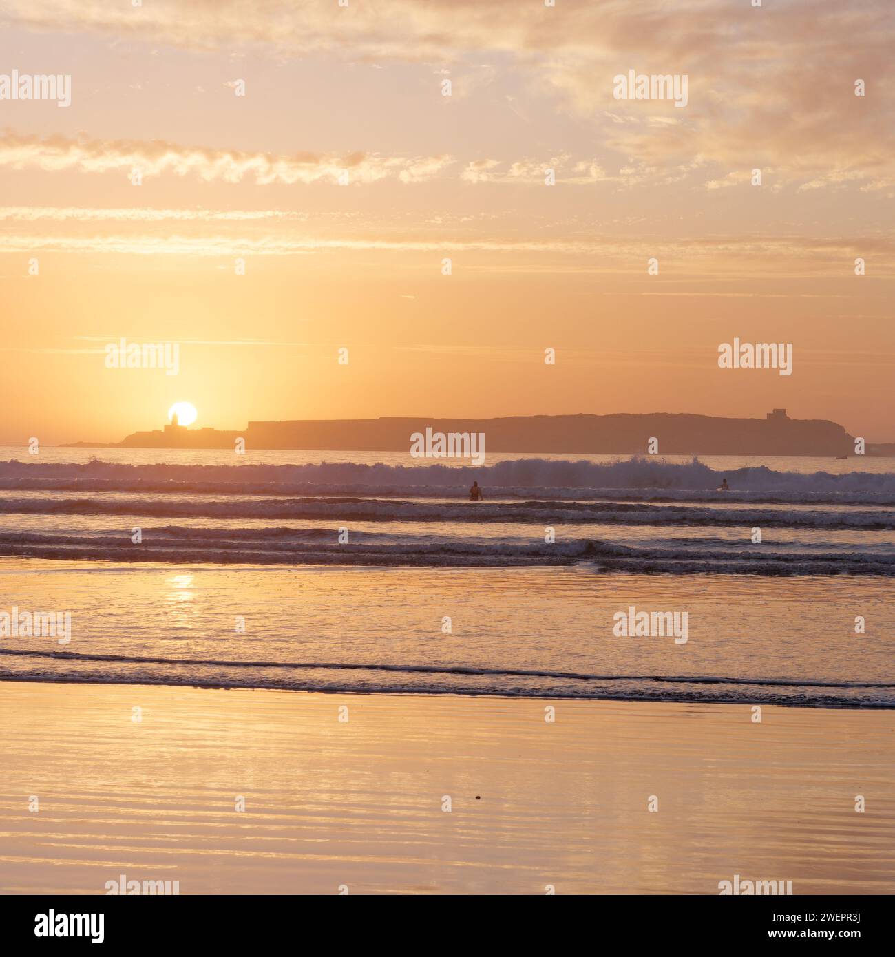 Menschen, die im Meer baden, mit Insel dahinter bei Sonnenuntergang in Essaouira, Marokko, 26. Januar 2024 Stockfoto