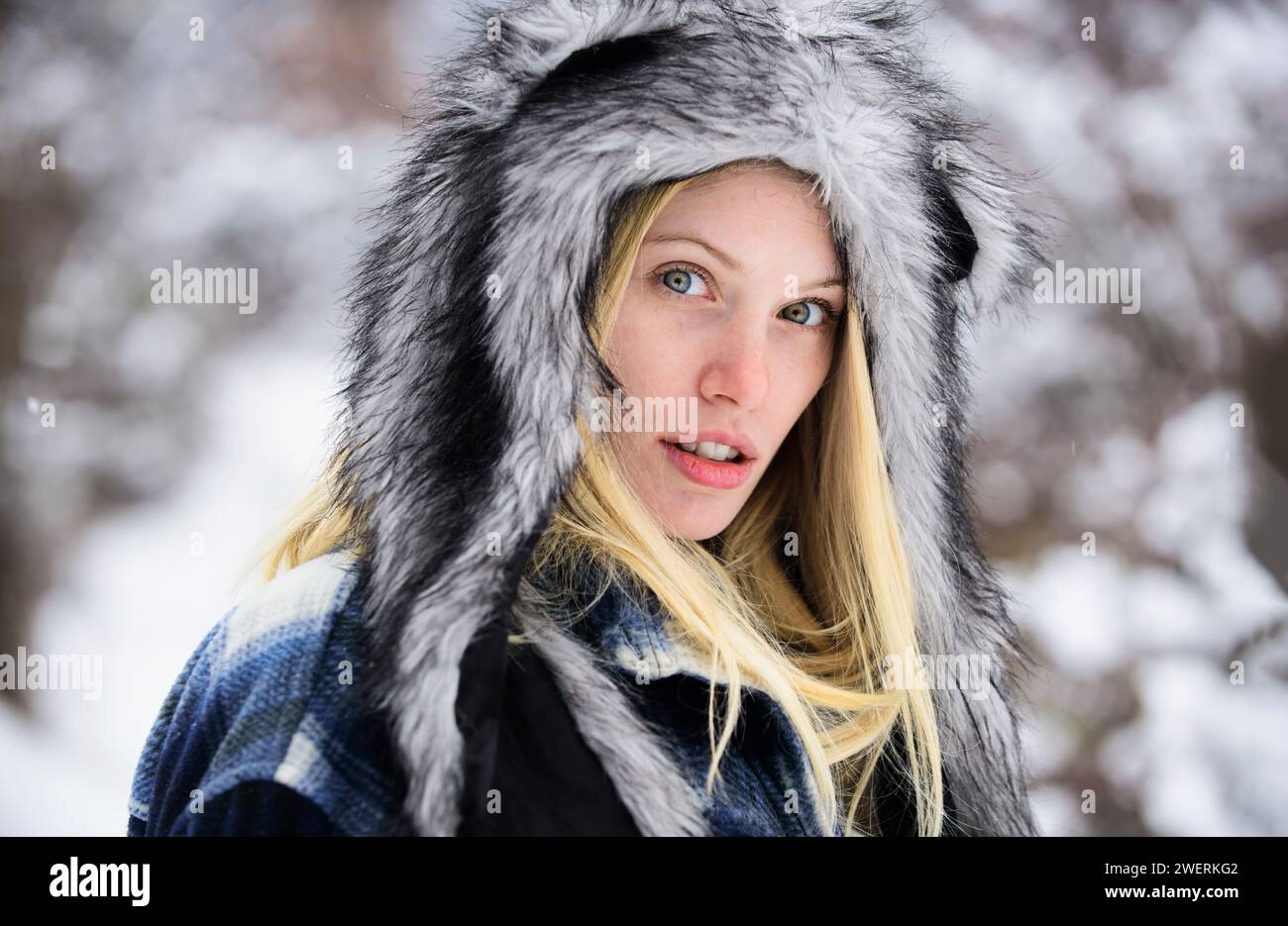 Winterzeit. Nahaufnahme-Porträt eines blonden Mädchens mit stilvollem Pelzhut am schneebedeckten Wintertag. Schöne junge Frau in kariertem Mantel und warmer Hut geht im Winter Stockfoto