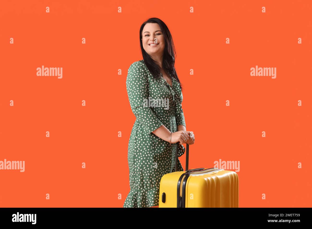 Schöne glückliche reife Frau mit Koffer auf orangem Hintergrund. Internationaler Frauentag Stockfoto