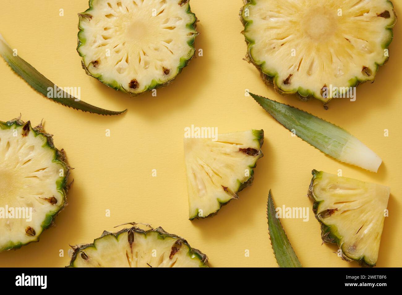 Frische Ananas (Ananas comosus) Scheiben, Kreise und Dreiecke, grüne Blätter verziert auf gelbem Hintergrund. Werbefoto, Ananas ist reich an V Stockfoto