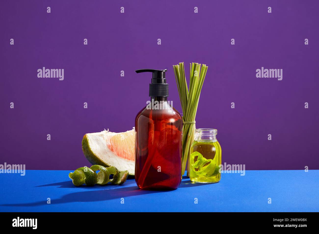 Mockup-Szene mit leerer Flasche für Kosmetik von rosa Pomelo und Zitronengras-Extrakt auf violettem Hintergrund. Szene für Werbung für Bio-Kosmetik. Esse Stockfoto