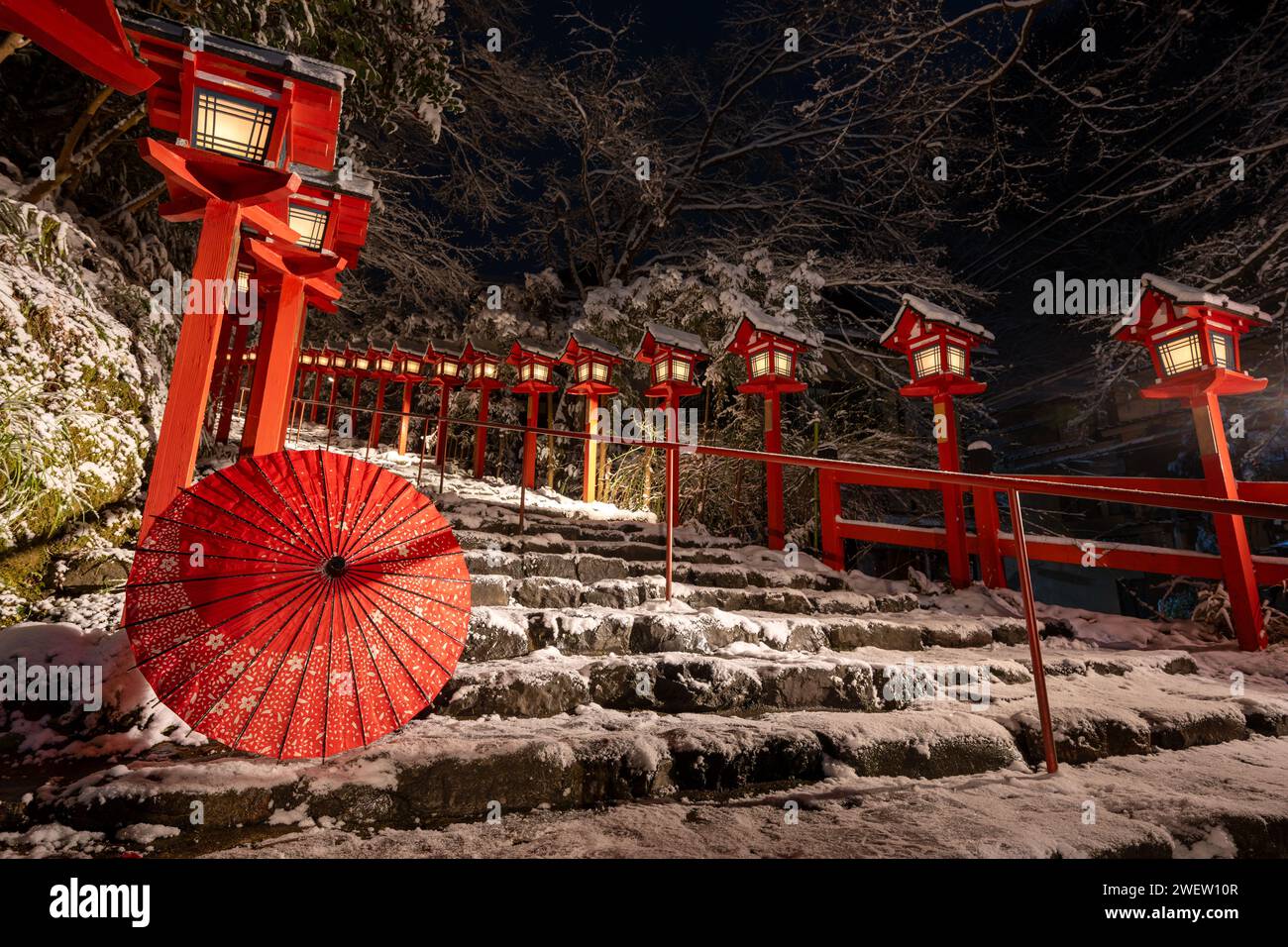 Schnee in Kyoto, Japan. Kifune-Schrein traditioneller Lichtmast in verschneite Winternacht. Japanischer Regenschirm auf der Steintreppe. Das Konzept der japanischen Kultur. Stockfoto