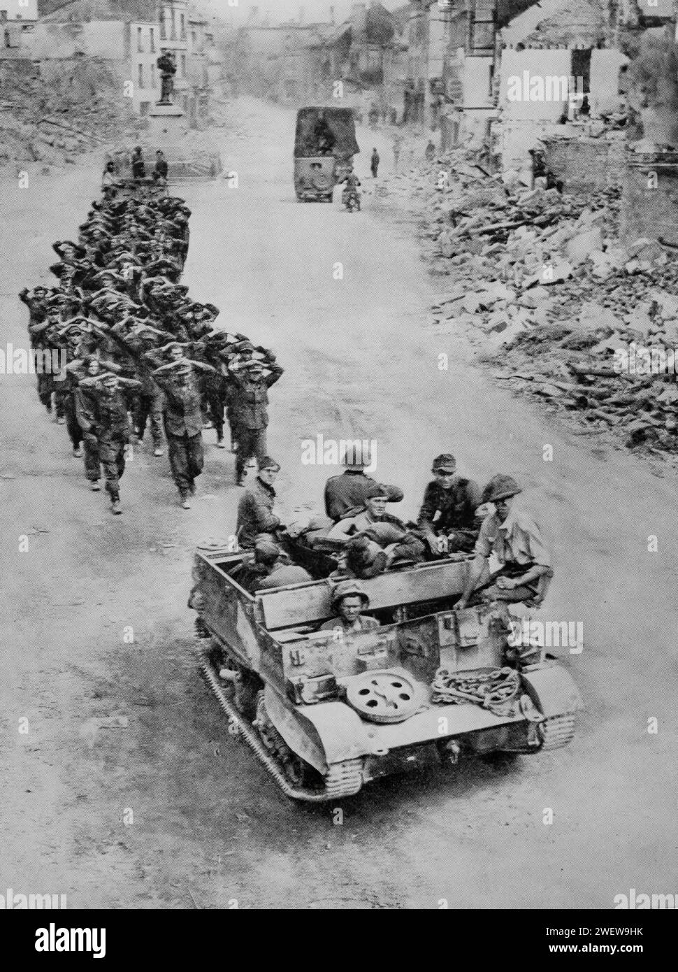 Deutsche Gefangene, die von Truppen begleitet werden, durchqueren Mitte August 1944 die Ruinen einer Stadt in der Normandie, während des Zweiten Weltkriegs nach der Invasion der Alliierten in Europa am D-Day am 6. Juni 1944. Stockfoto