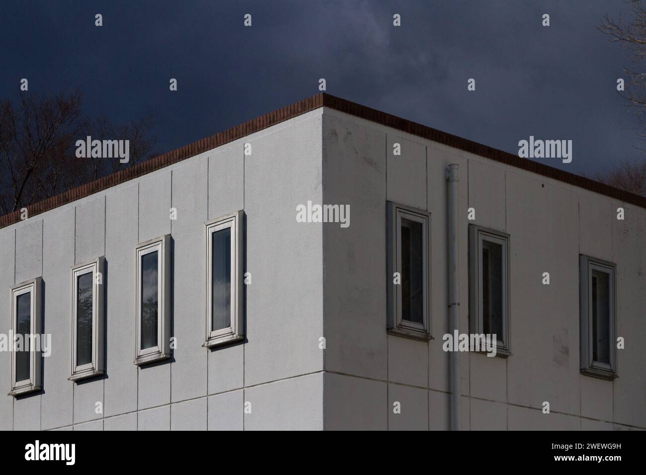 Ein unscheinbares quadratisches weißes Betongebäude mit dünnen Fenstern unter einem glühenden Himmel. Kanagawa, Japan. Stockfoto
