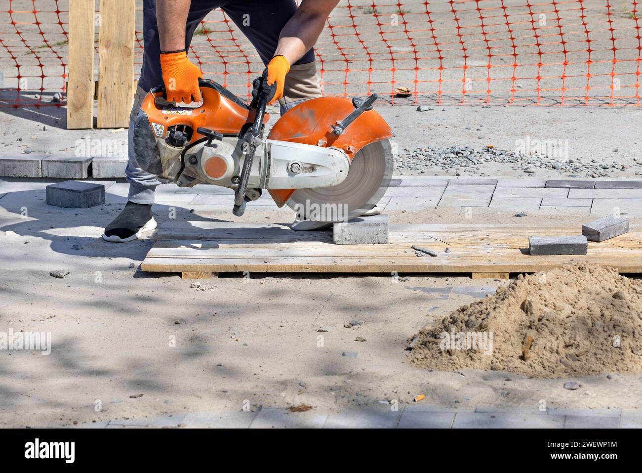 Ein Arbeiter schneidet Pflasterplatten auf einer Holzpalette mit einem manuellen Gasschneider mit einer Diamantklinge an einem klaren Sommertag. Kopierbereich. Stockfoto