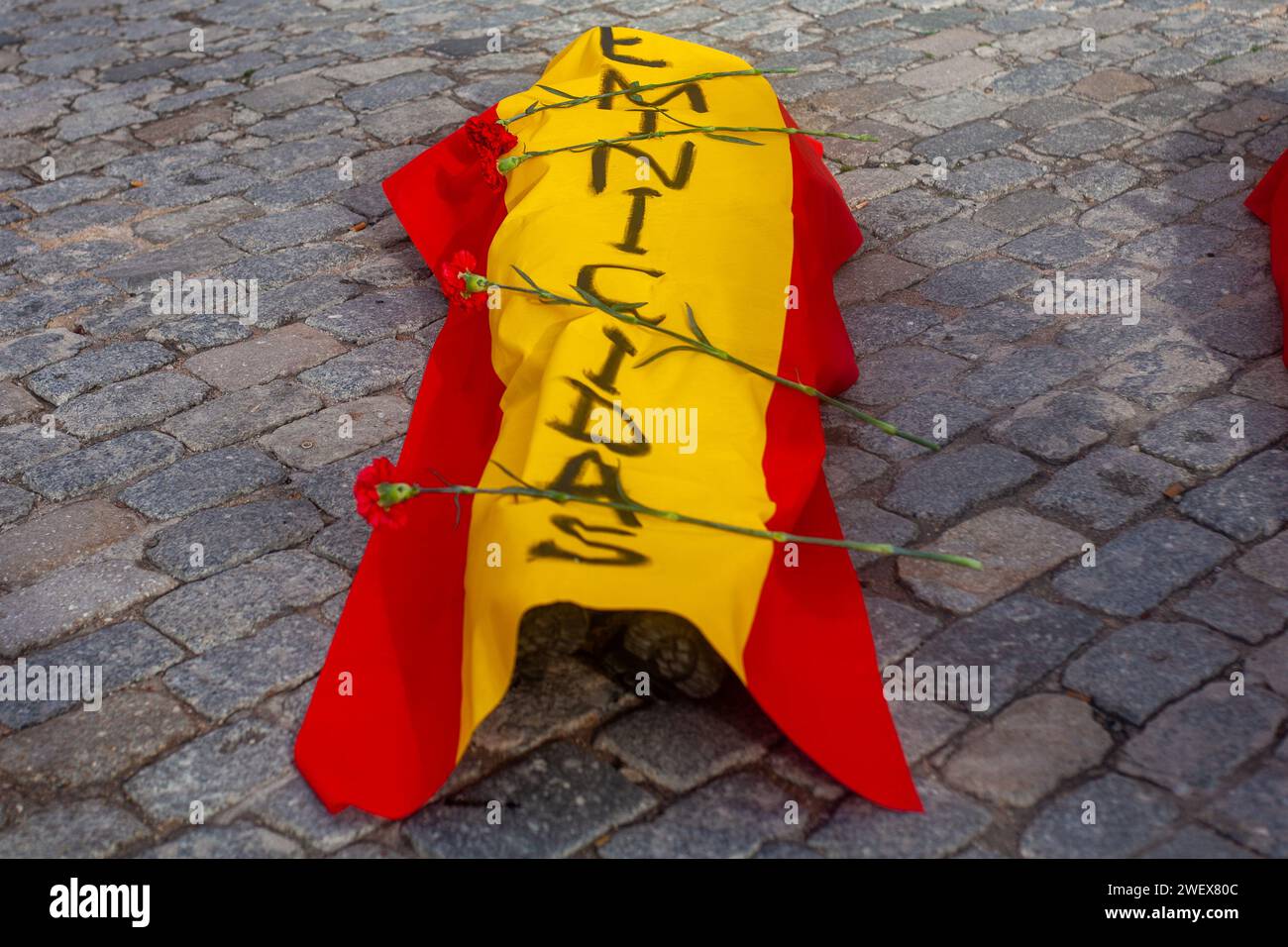 Madrid, Spanien. Januar 2024. Eine Aktivistin von femen Spain liegt auf dem Boden, während sie mit einer spanischen Flagge bedeckt ist, eine Performance, die Gräber von Frauen simuliert, die Opfer sexistischer Gewalt sind, während einer Aktion im Zentrum von Madrid. Aktivisten von Femen España führten eine Aktion durch, um die Frauenmorde und den sexistischen Leugnungskrieg der spanischen konservativen Sektoren anzuprangern. Die Aktion fand auf der Plaza de San Andrés in Madrid statt. Quelle: SOPA Images Limited/Alamy Live News Stockfoto