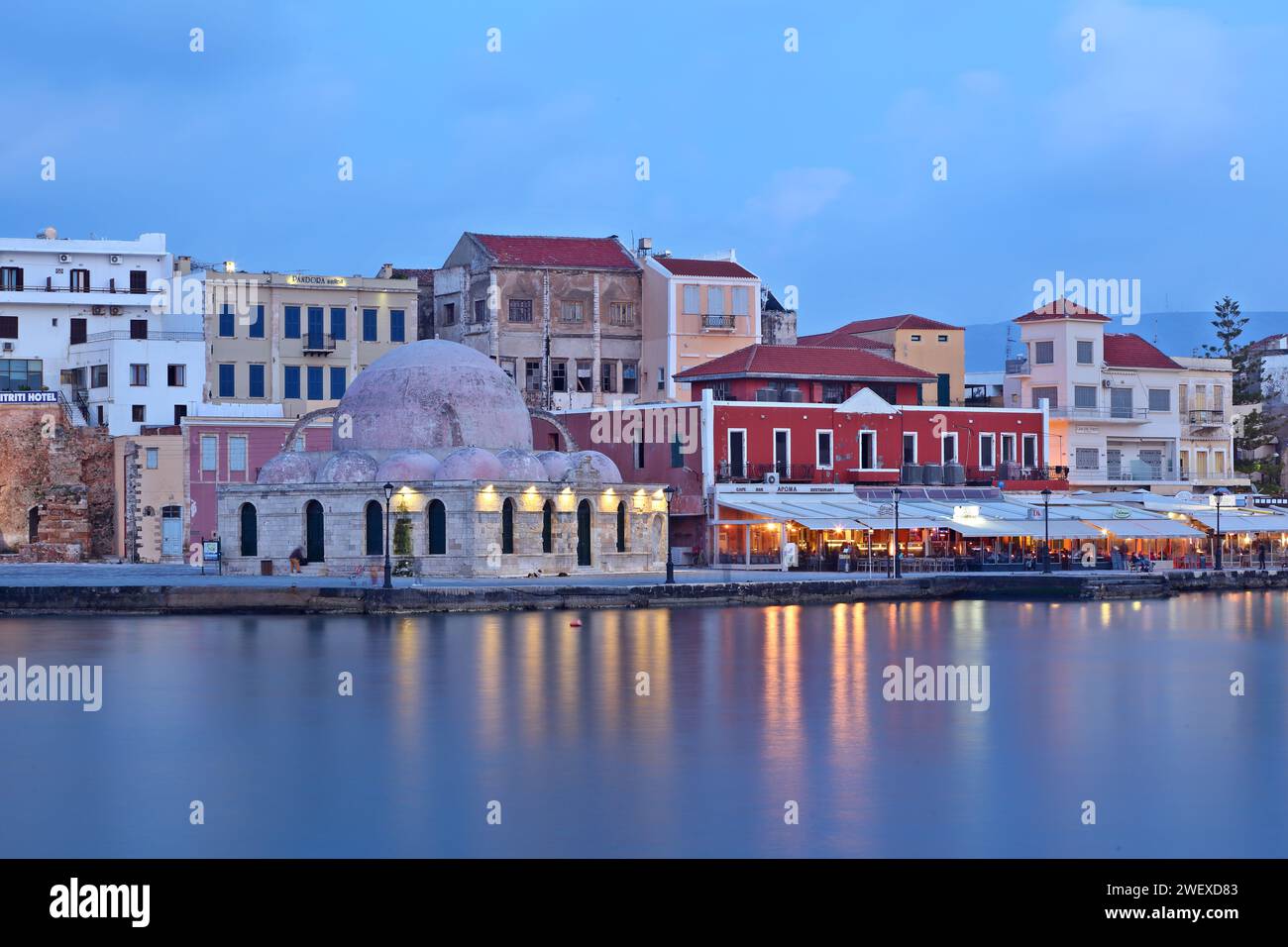 Blick auf den alten Hafen von Chania, Insel Kreta, mit seinen bunten Häusern, dem alten Hamman im Vordergrund und Lichtern Reflexionen auf seidenem Wasser Stockfoto