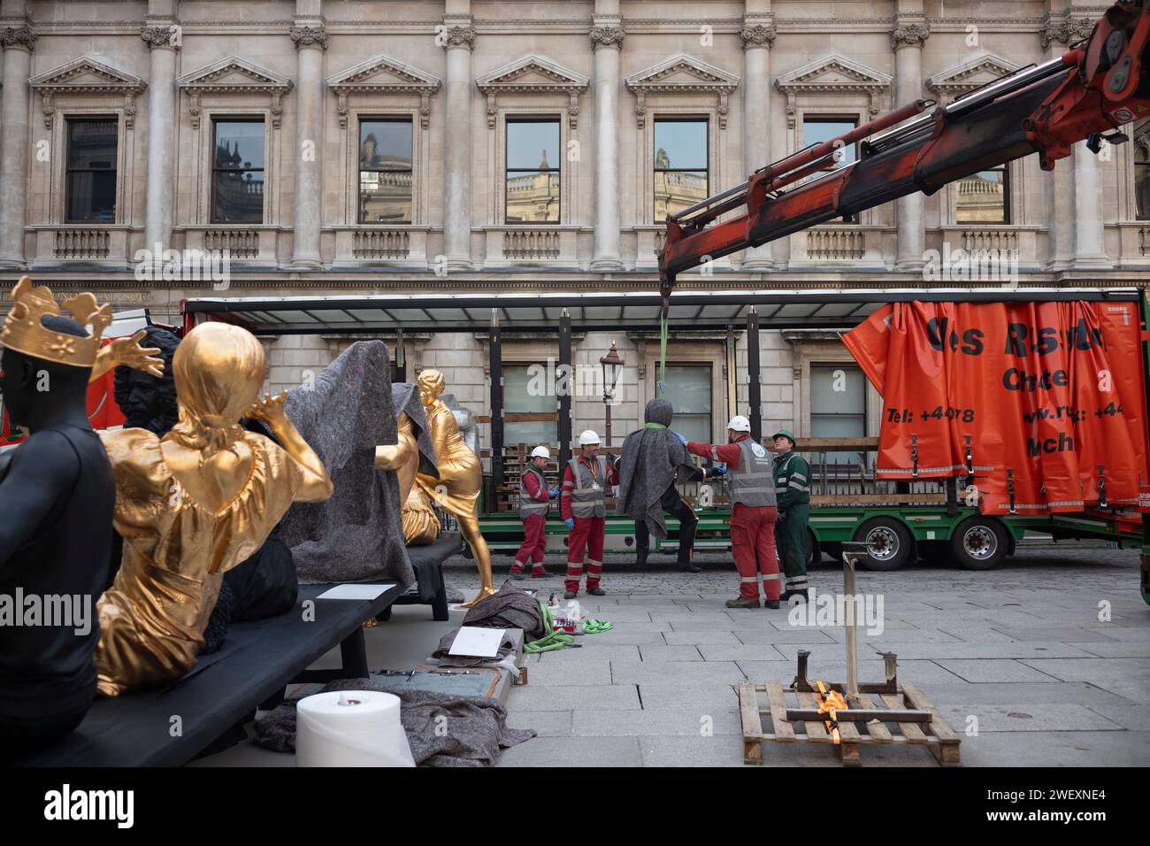 London, Großbritannien. Januar 2024. Tavares Strachans monumentale Skulpturen „das erste Abendmahl“ aus Bronze, schwarzer Patina und Blattgold im Hof der Royal Academy. Im Februar 2024 bringen die Arbeiter die letzte Skulpturenfigur auf den Hof der Akademie vor der Unvielfalt in Position. Die Skulptur des interdisziplinären Künstlers Tavares Strachan (*1979 Nassau, die Bahamas), im Rahmen der Ausstellung Enangled Pasts: 1768 - Now: Art, Colonialism and Change. Januar 2024. Royal Academy, Piccadilly, London, England, Vereinigtes Königreich Credit: Clickpics/Alamy Live News Stockfoto