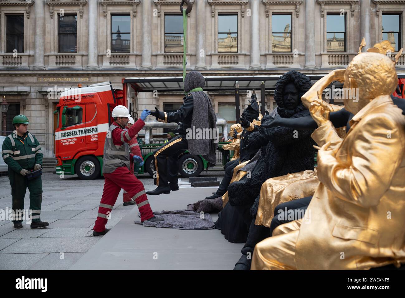 London, Großbritannien. Januar 2024. Tavares Strachans monumentale Skulpturen „das erste Abendmahl“ aus Bronze, schwarzer Patina und Blattgold im Hof der Royal Academy. Im Februar 2024 bringen die Arbeiter die letzte Skulpturenfigur auf den Hof der Akademie vor der Unvielfalt in Position. Die Skulptur des interdisziplinären Künstlers Tavares Strachan (*1979 Nassau, die Bahamas), im Rahmen der Ausstellung Enangled Pasts: 1768 - Now: Art, Colonialism and Change. Januar 2024. Royal Academy, Piccadilly, London, England, Vereinigtes Königreich Credit: Clickpics/Alamy Live News Stockfoto