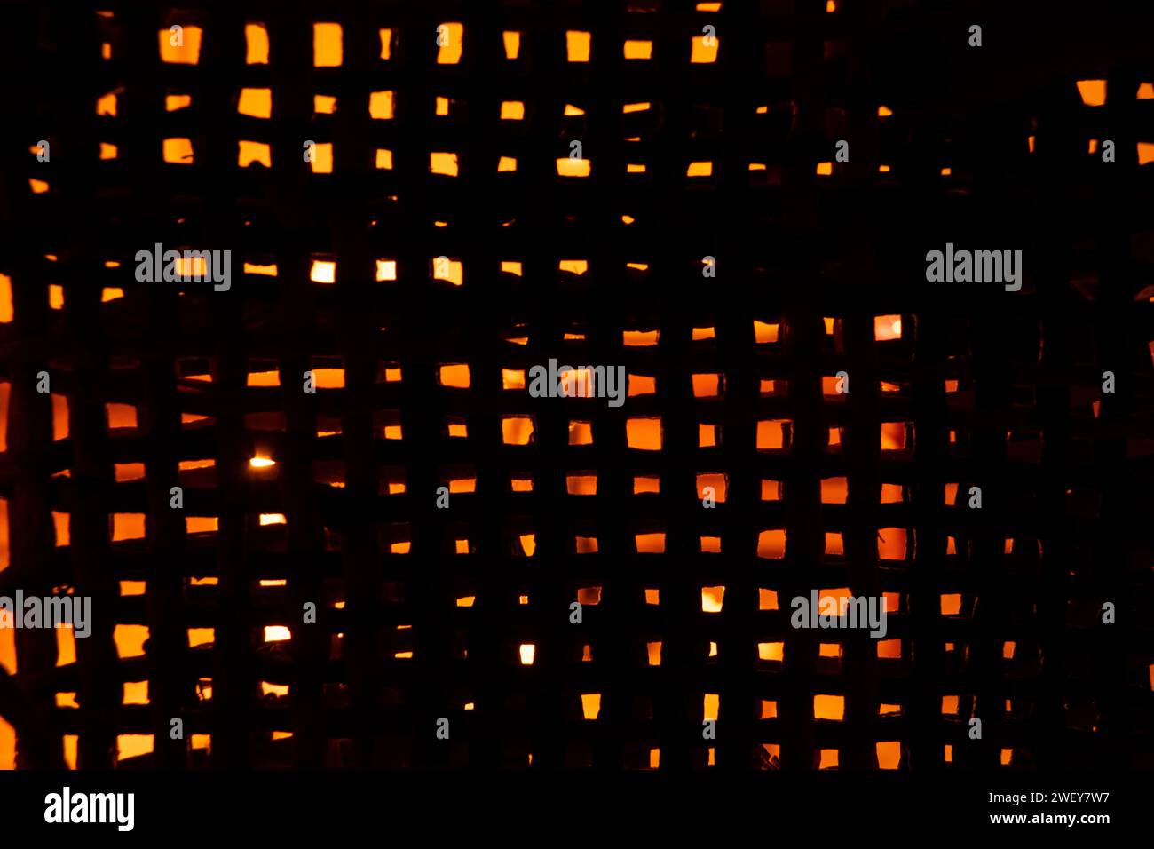 Das Licht einer Kerze ist durch ein feines Stroh-Netz im Dunkeln sichtbar, Hintergrund, Netz für Hintergrund Stockfoto