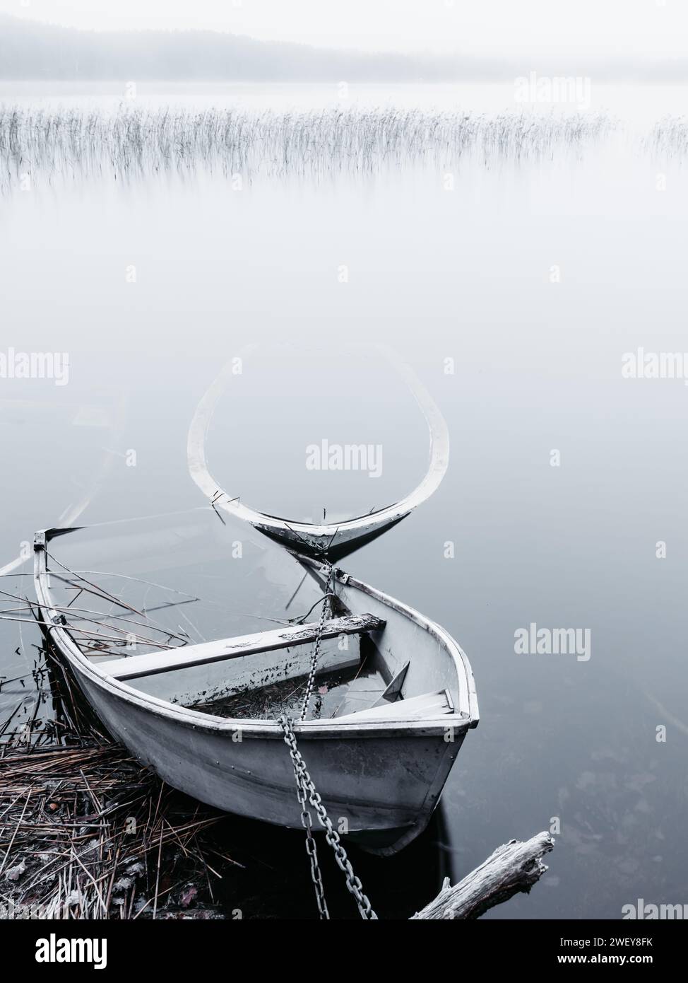 Zwei einsame Boote ruhen auf dem ruhigen Wasser eines Sees, umgeben von dem ruhigen Nebel eines frühen morgens. Stockfoto