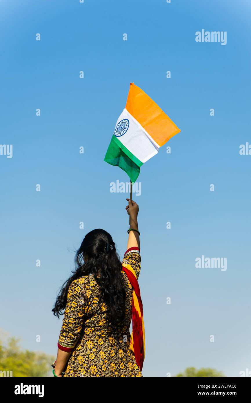 Ein junges indianermädchen, das die indische Nationalflagge hält und tagsüber mit hellblauem Himmel winkt Stockfoto