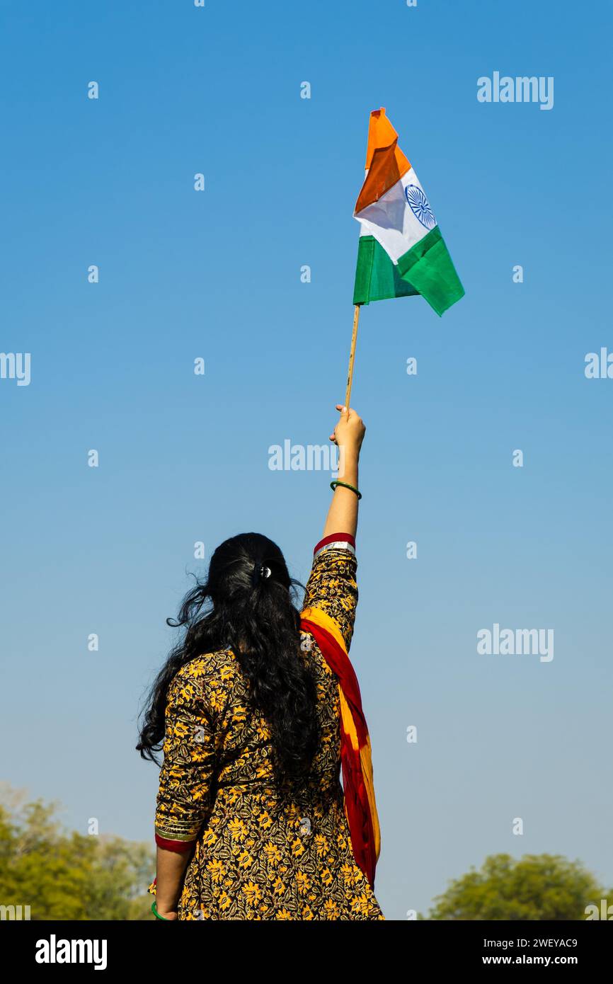 Ein junges indianermädchen, das die indische Nationalflagge hält und tagsüber mit hellblauem Himmel winkt Stockfoto