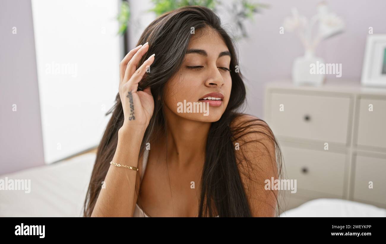 Eine ruhige südasiatische Frau genießt einen Moment der Ruhe in ihrem minimalistischen Schlafzimmer. Stockfoto