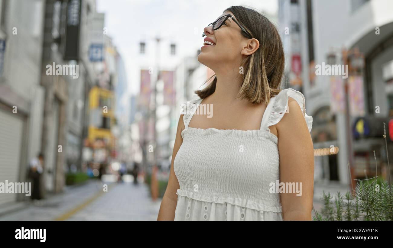 Schönheit, atemberaubende Erwachsene hispanische Frau mit Brille und Blick auf das pulsierende Stadtbild tokios. Dieser brünette Tourist ist fasziniert von Stockfoto