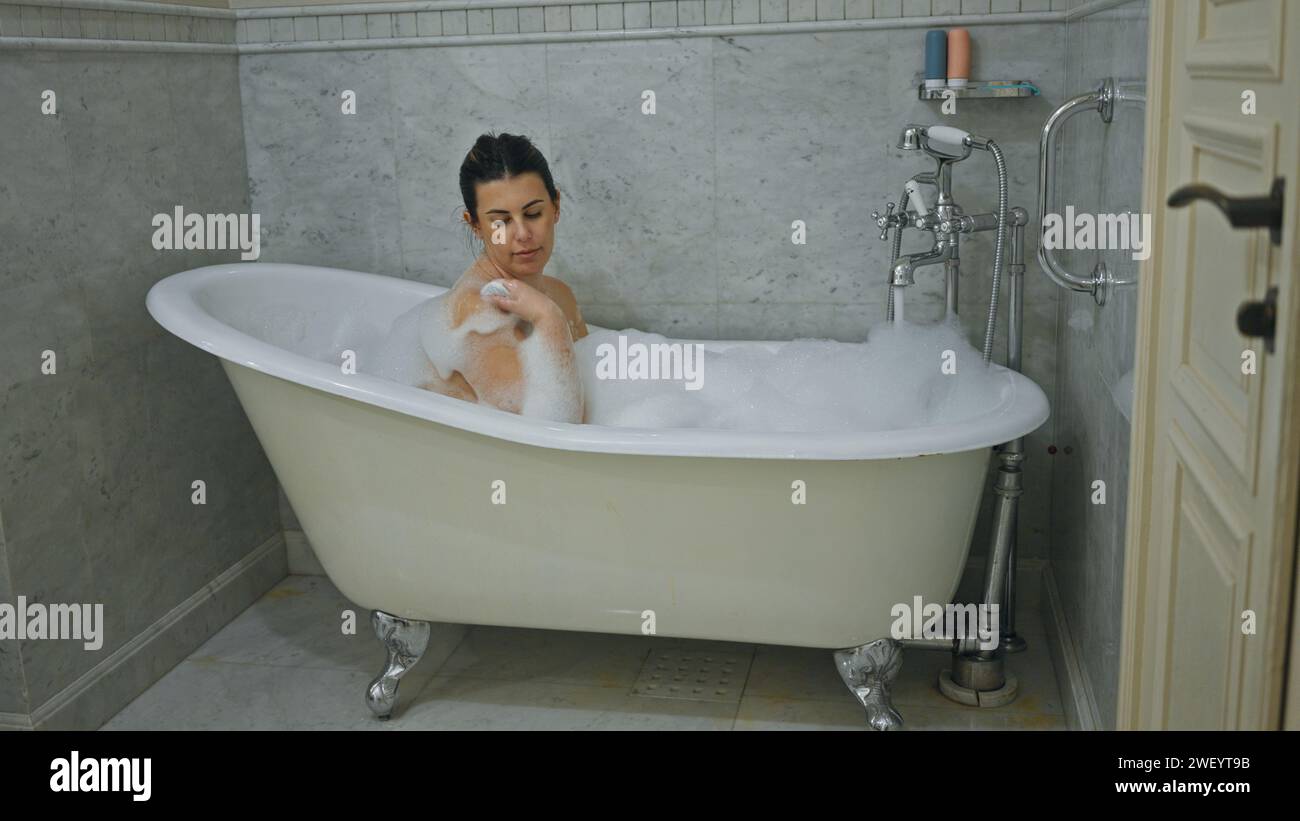 Eine entspannte Frau genießt ein Sprudelbad in einer eleganten Badewanne mit Klauenfuß in einem Marmorbadezimmer Stockfoto