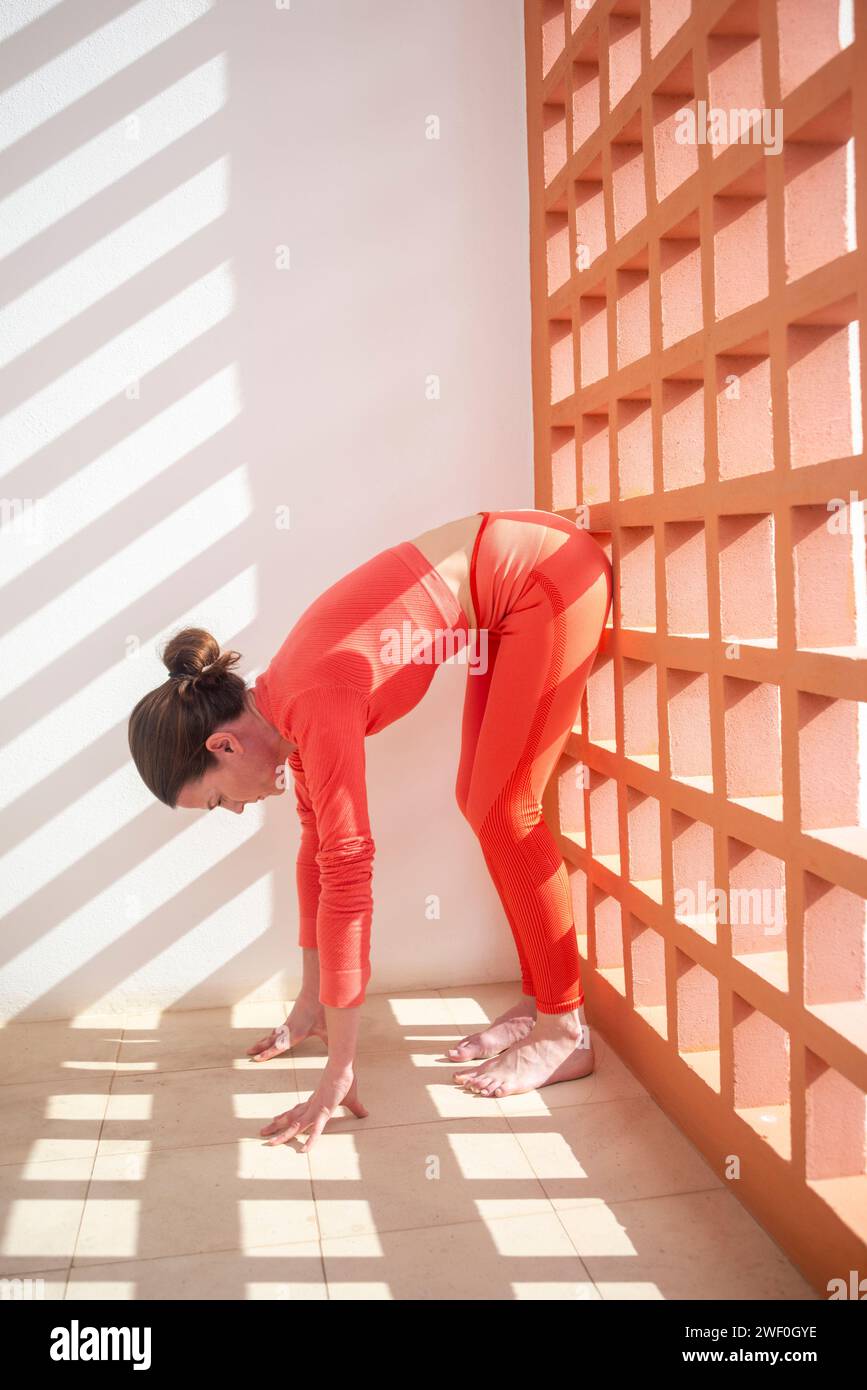 Sportliche Frau, die eine Dehnung im Stehen nach vorne macht, Wand Pilates Übungen. Stockfoto