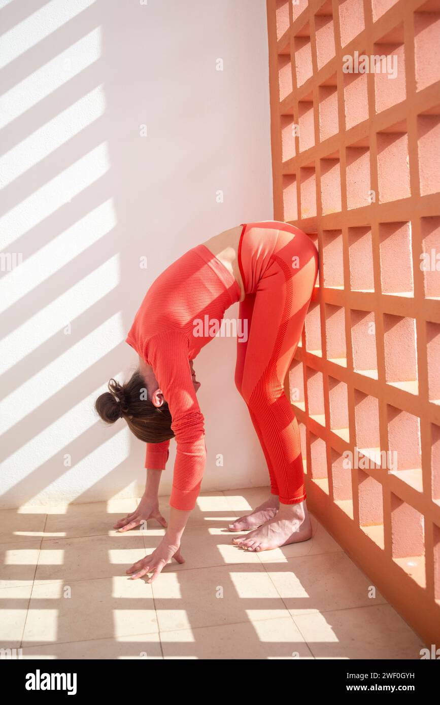 Sportliche Frau, die eine Dehnung im Stehen nach vorne macht, Wand Pilates Übungen. Stockfoto