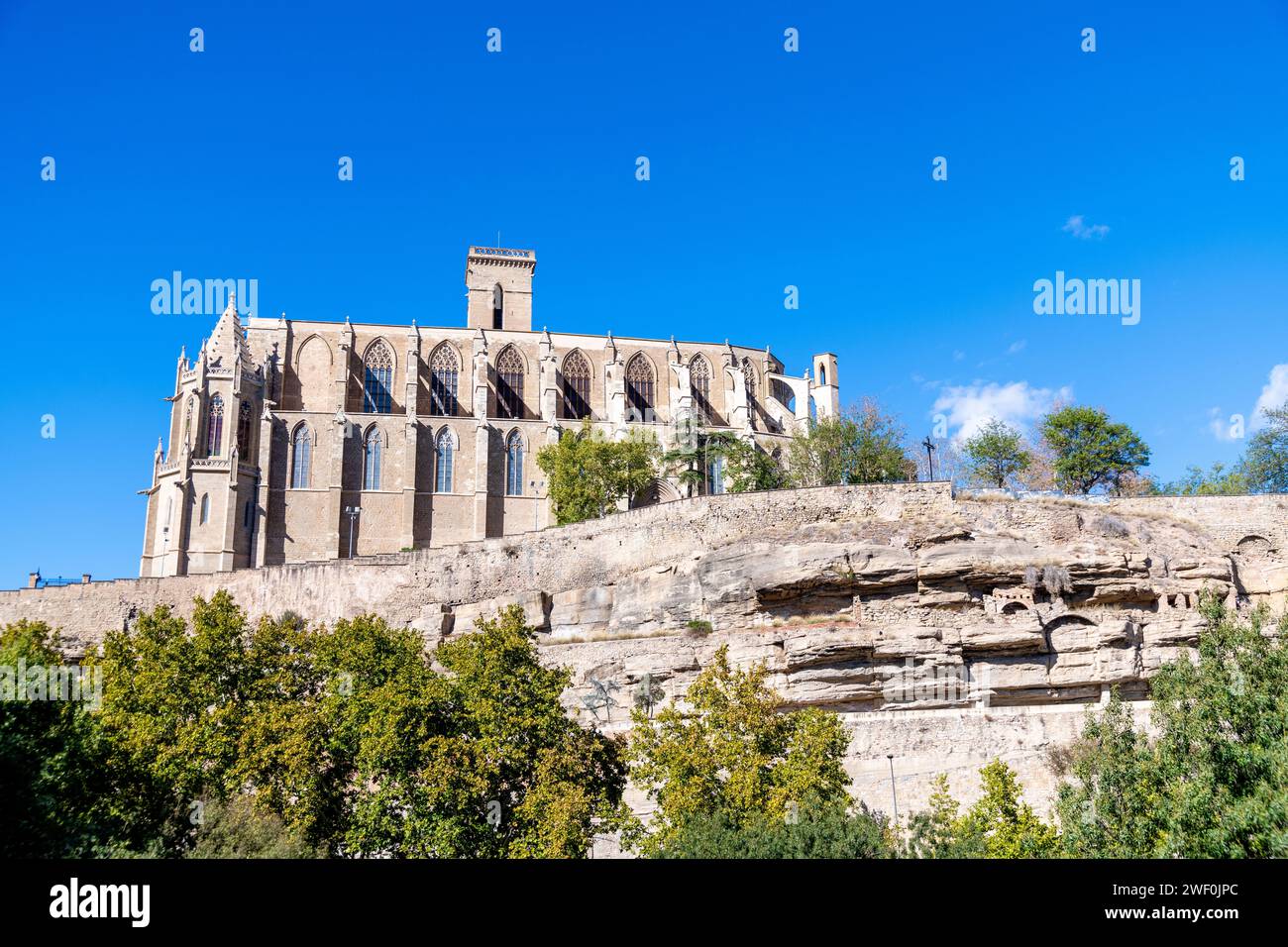 Hinter der Basilika Santa Maria de La Seu in der Sonne und hellen Wolken mit Bäumen und Felsen im Vordergrund Stockfoto