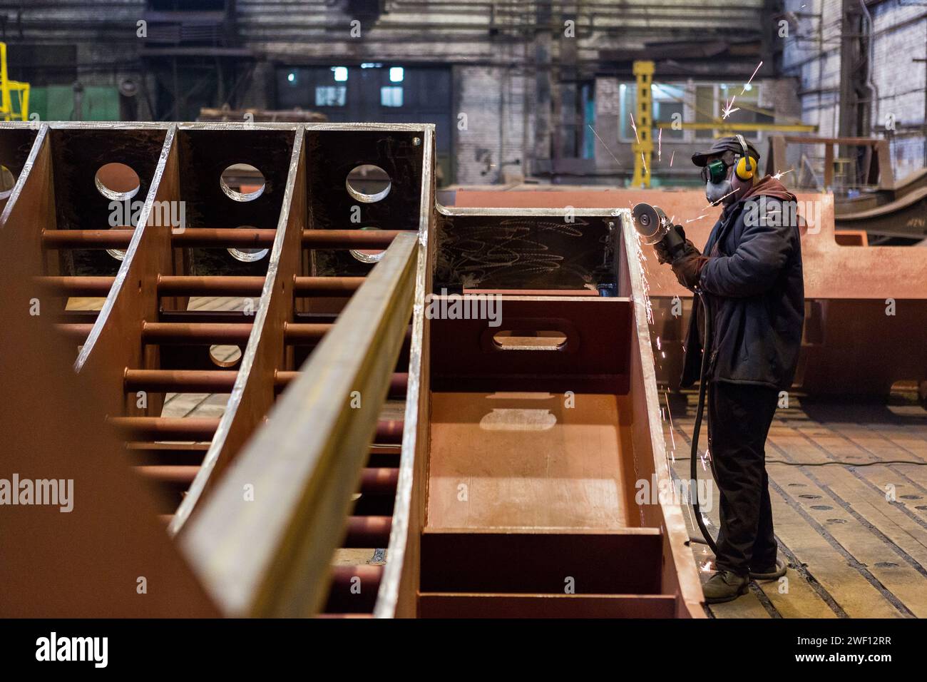 Der Arbeiter in einer Maske schleift ein Metallteil in einer Fabrik oder schneidet es mit einer elektrischen Kreissäge. Stockfoto