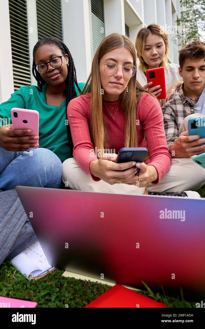 Eine Gruppe junger multirassischer Universitätsstudenten tauchte abhängig von ihrer Mobilzellentechnologie ein Stockfoto