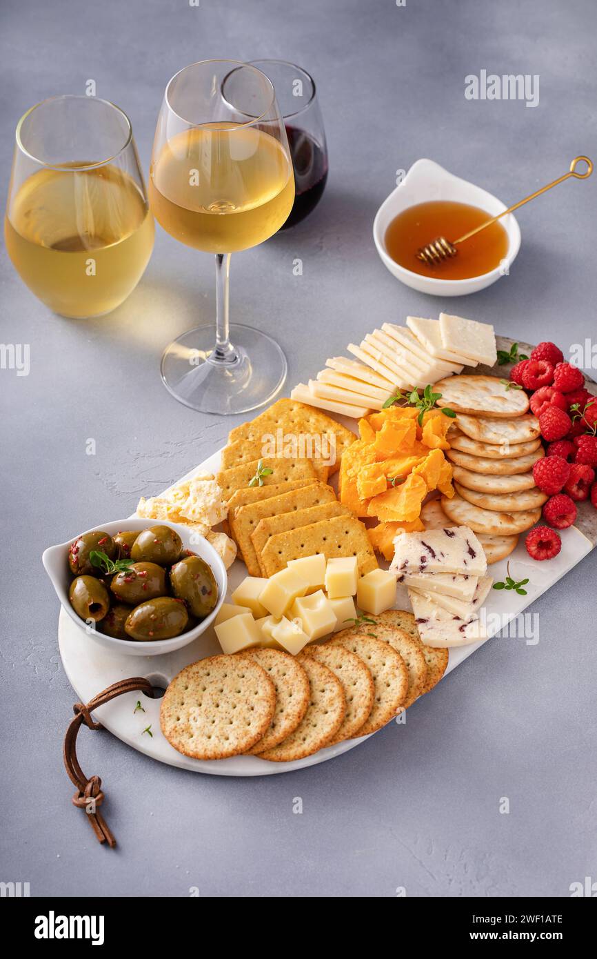 Kleiner Käse und Crackerbrett mit frischen Beeren und Oliven serviert mit Honig und mehreren Gläsern Wein Stockfoto