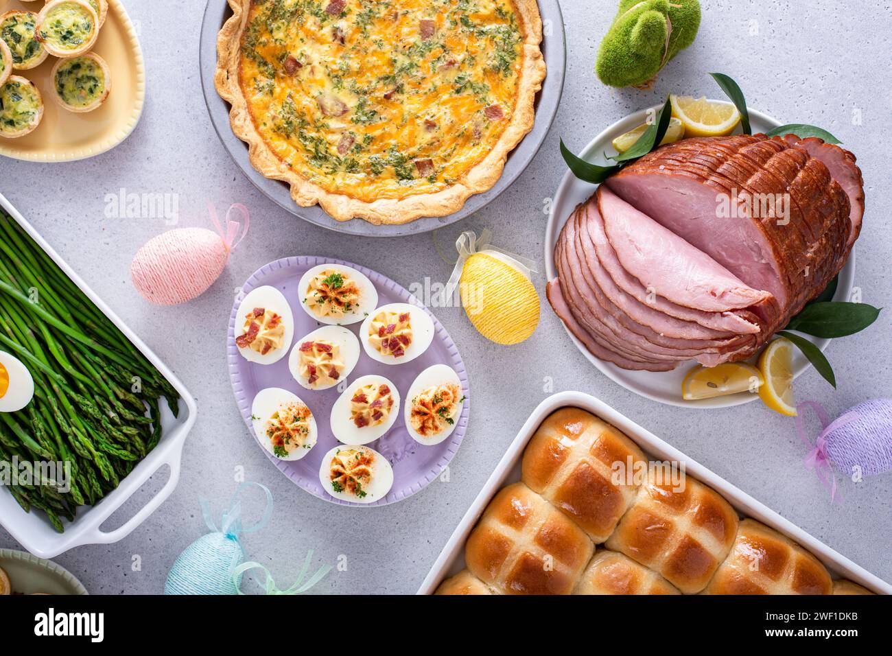 Osterbrunch auf einem großen Tisch mit spiralförmigem Schinken, Quiche, Eiern und heißen Kreuzbrötchen mit Osterdekor Stockfoto