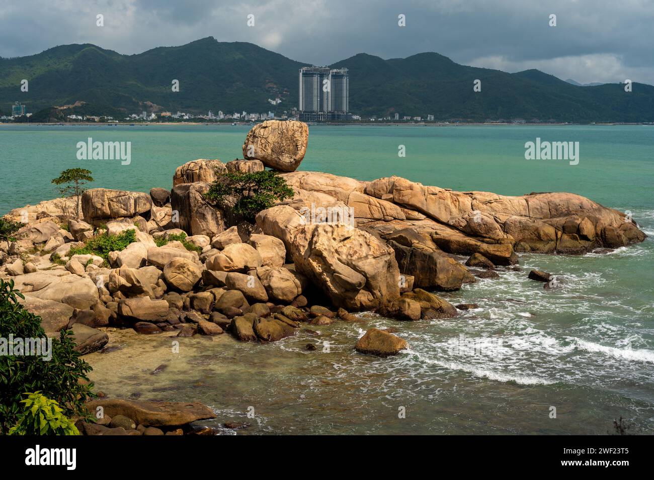 Nha Trang, Vietnams Küstenlandschaft entfaltet sich tagsüber in einem lebhaften Spektakel. Steine und goldener Sand treffen unter strahlender Sonne auf azurblaues Meer und schaffen ein Bild Stockfoto