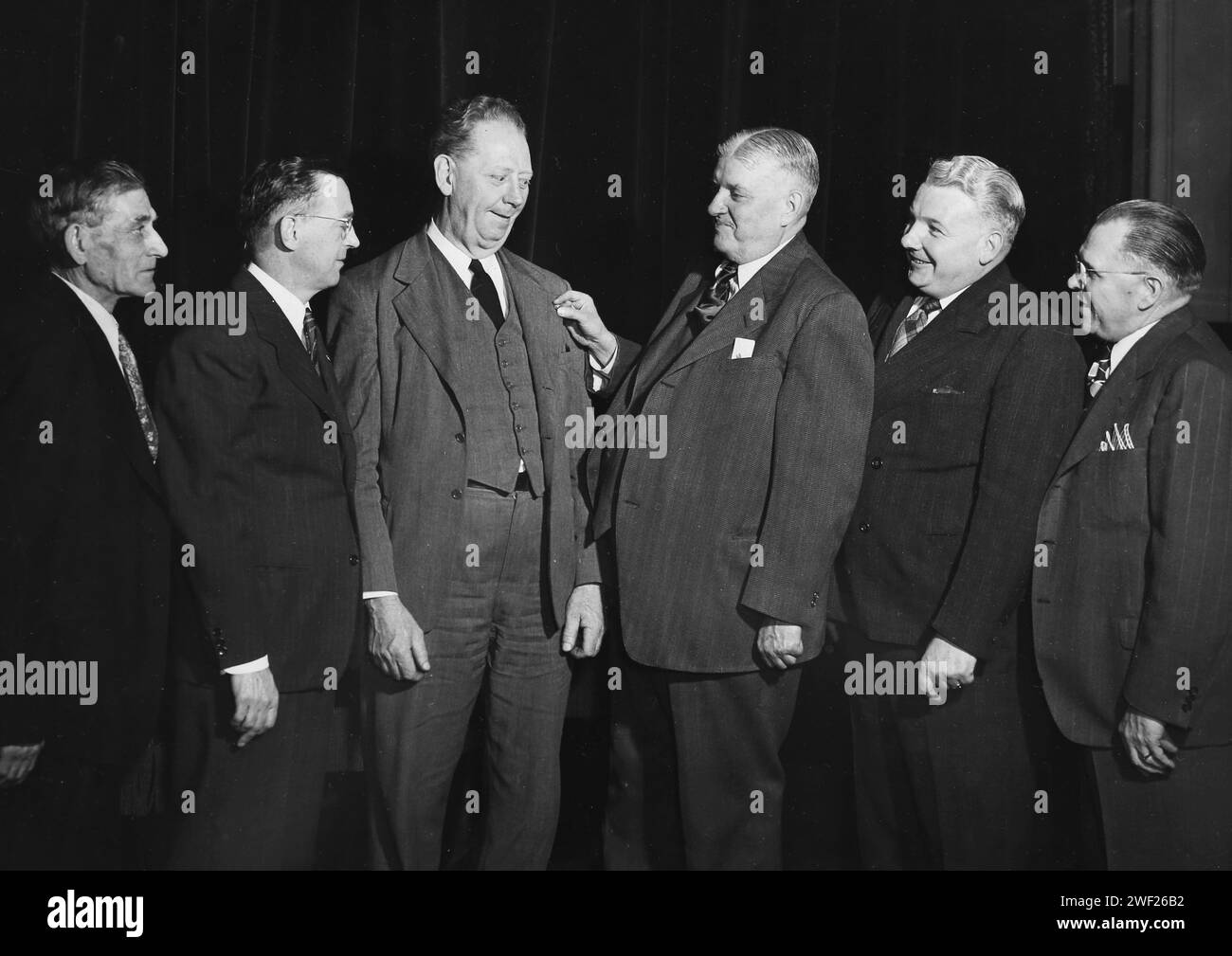 Geschäftsmännertypen stehen an, um die Verleihung einer neuen Anstecknadel für einen ihrer Art zu bewundern, CA. 1940. Stockfoto