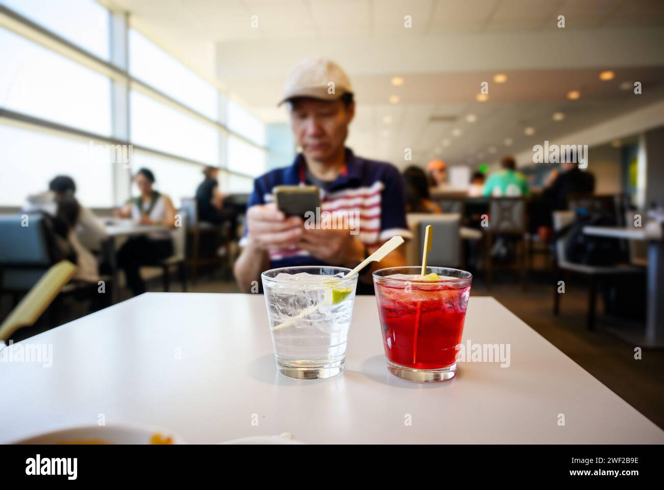 Die Gäste genießen Snacks und Getränke in der Flughafenlounge. Ein Mann, der sein Smartphone überprüft, Cocktails auf dem Tisch. Stockfoto