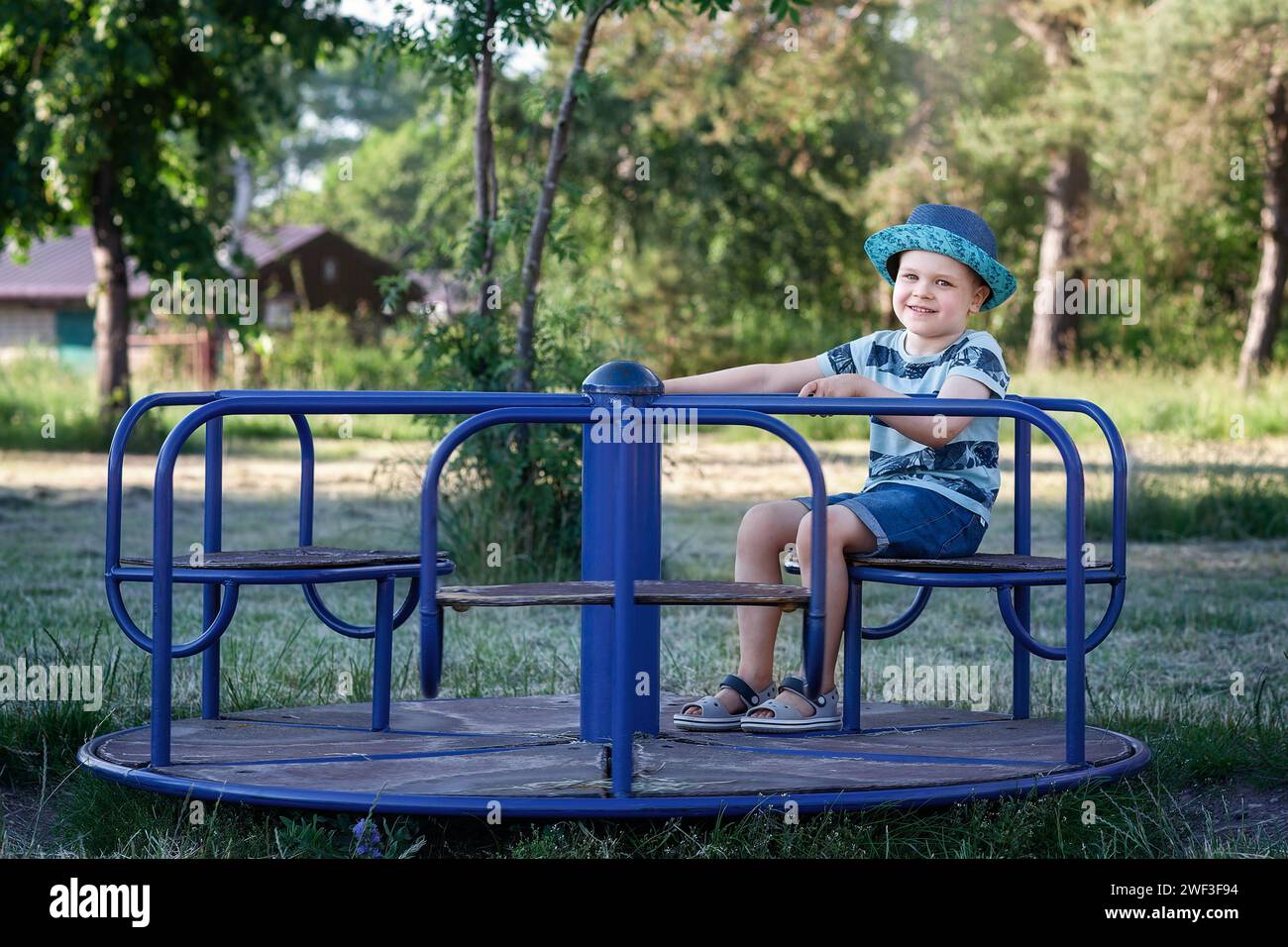 Ein vierjähriger Junge in blauer Kleidung dreht sich auf dem Spielplatzkarussell. Stockfoto