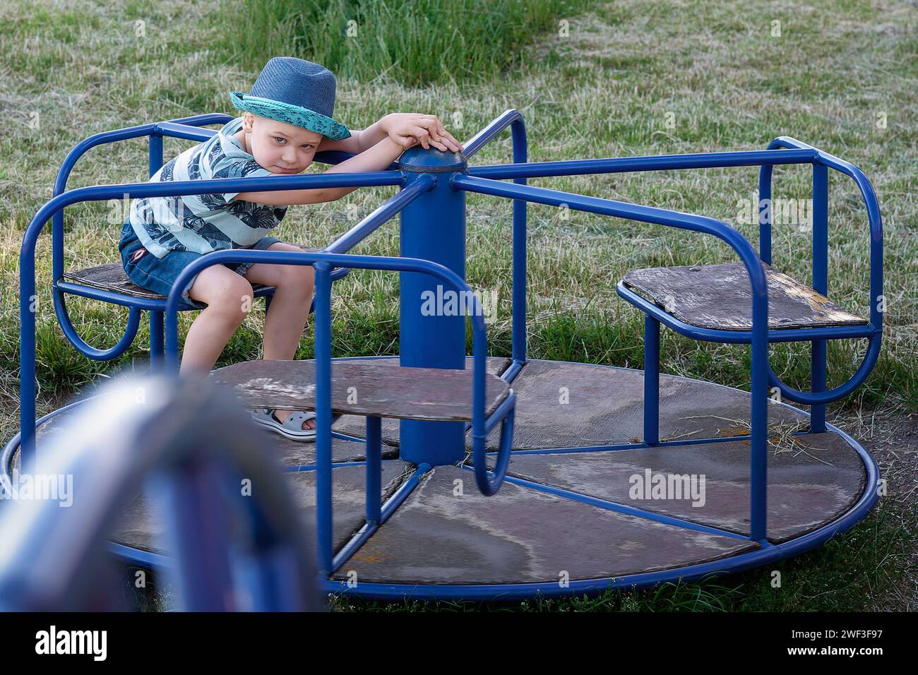 Spielplatz im Freien Karussell und süßer Junge, der darauf sitzt und posiert. Stockfoto