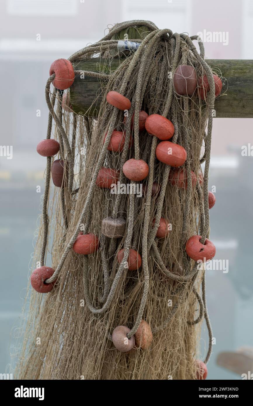 Eine Reihe von Fischernetzen hing in der Nähe des Hafens in der Nähe von Fischerbooten nach einem Angelausflug. Netze, verbunden mit Kunststoffseilen und Schwimmern in verschiedenen Farben Stockfoto