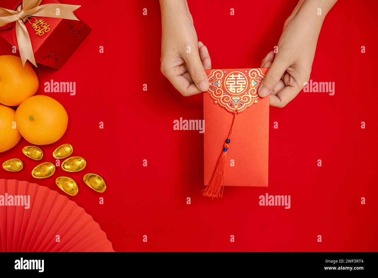 Flache Handlage, die den Tae EIA-Umschlag (roter Umschlag) von oben hält, um während der chinesischen Neujahrsfeier Geld zu geben. Roter Hintergrund Stockfoto