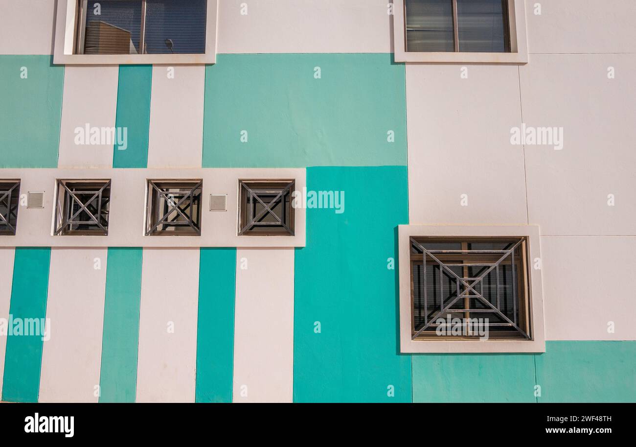 Grüne Streifen, die auf ein modernes Gebäude gemalt sind, mit quadratischen Fenstern und Sicherheitsgittern aus Metall. Stockfoto