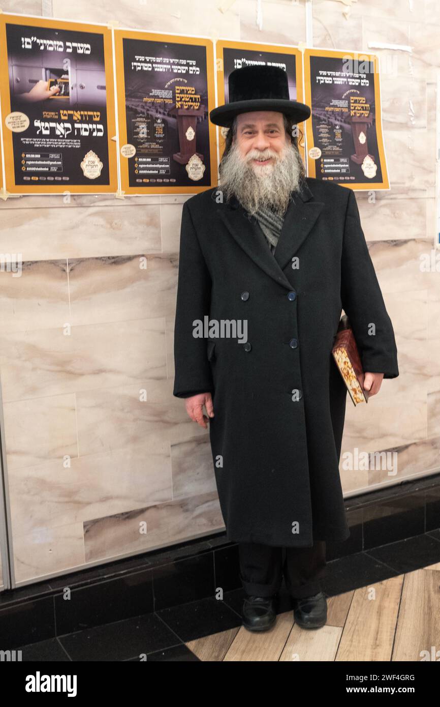 Ein älterer orthodoxer jüdischer Mann posiert für ein Fotobuch über Talmud und vor jiddischen Plakaten. In Brooklyn, New York. Stockfoto