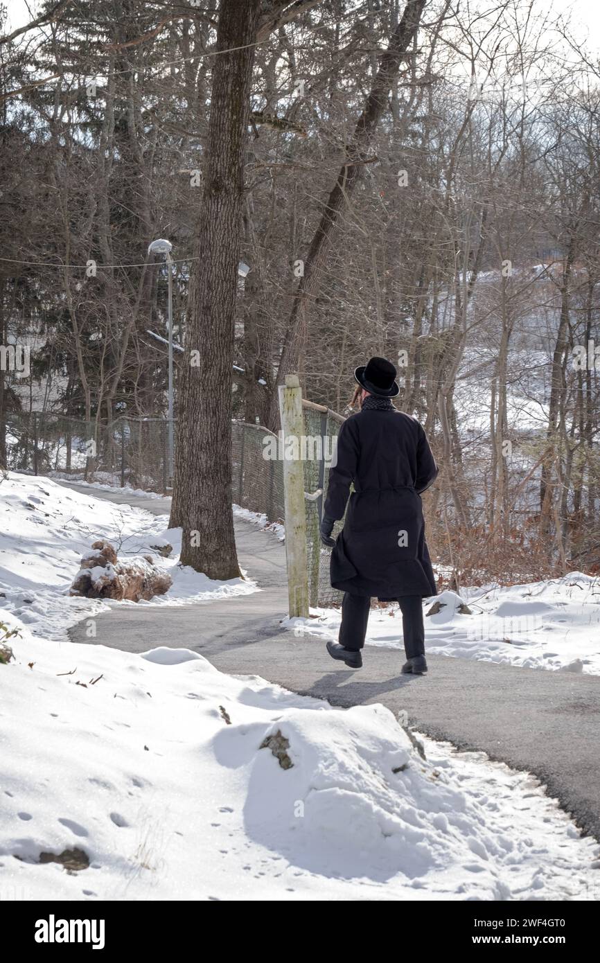 Ein nicht identifizierter orthodoxer jüdischer Mann in schwarz gekleidet geht im Winter 2024 auf einer gewundenen Straße in New York. Stockfoto