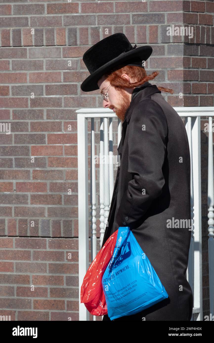 An einem windigen kalten Wintertag kauft ein chassidischer Jüd ein, während sein Peyus im Wind bläst. In Brooklyn, New York, 2024. Stockfoto