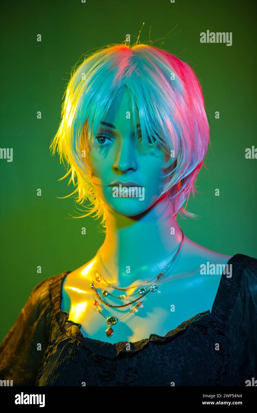 Plastikpuppe mit kurzen weißen Haaren, die in einem vier (4) Farben-Studio posiert, das rot-blau-gelb-grün leuchtet Stockfoto
