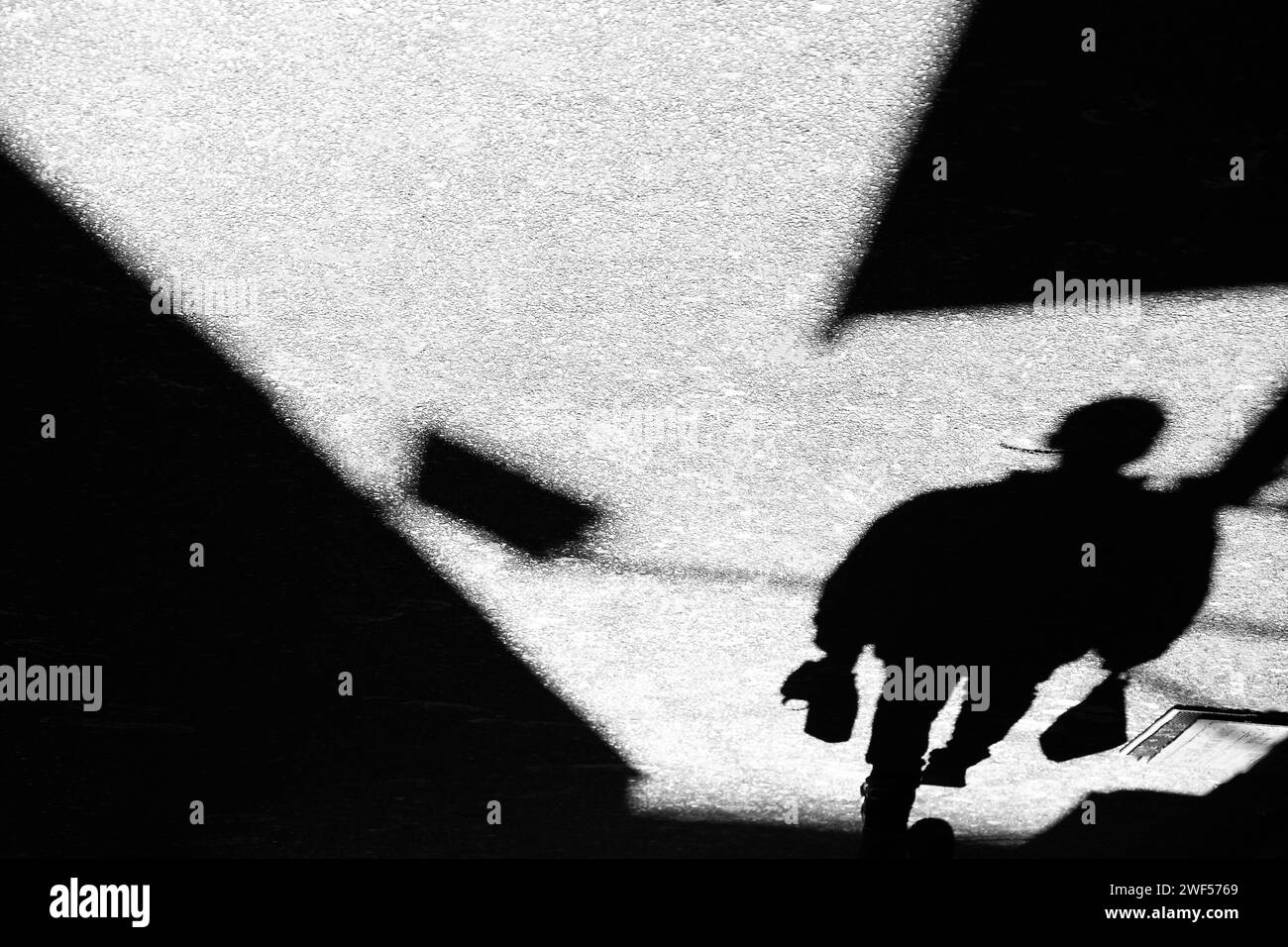 Schatten-Silhouette eines nicht erkennbaren Mannes, der in Schwarz-weiß mit Einkaufstaschen in der Gasse unterwegs ist Stockfoto